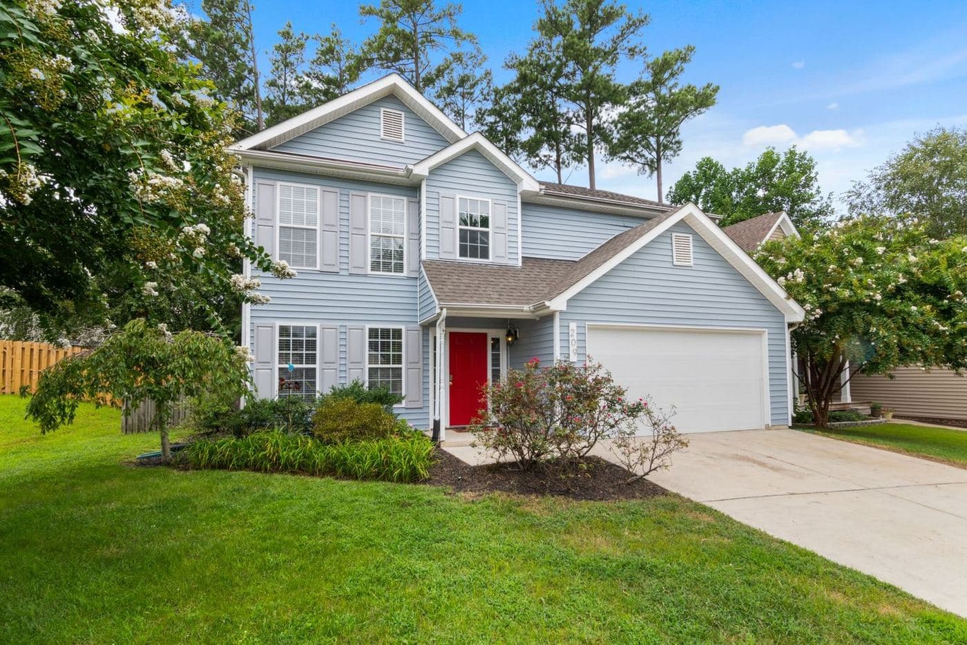 Blue two-story home with a red front door, attached garage and landscaped beds