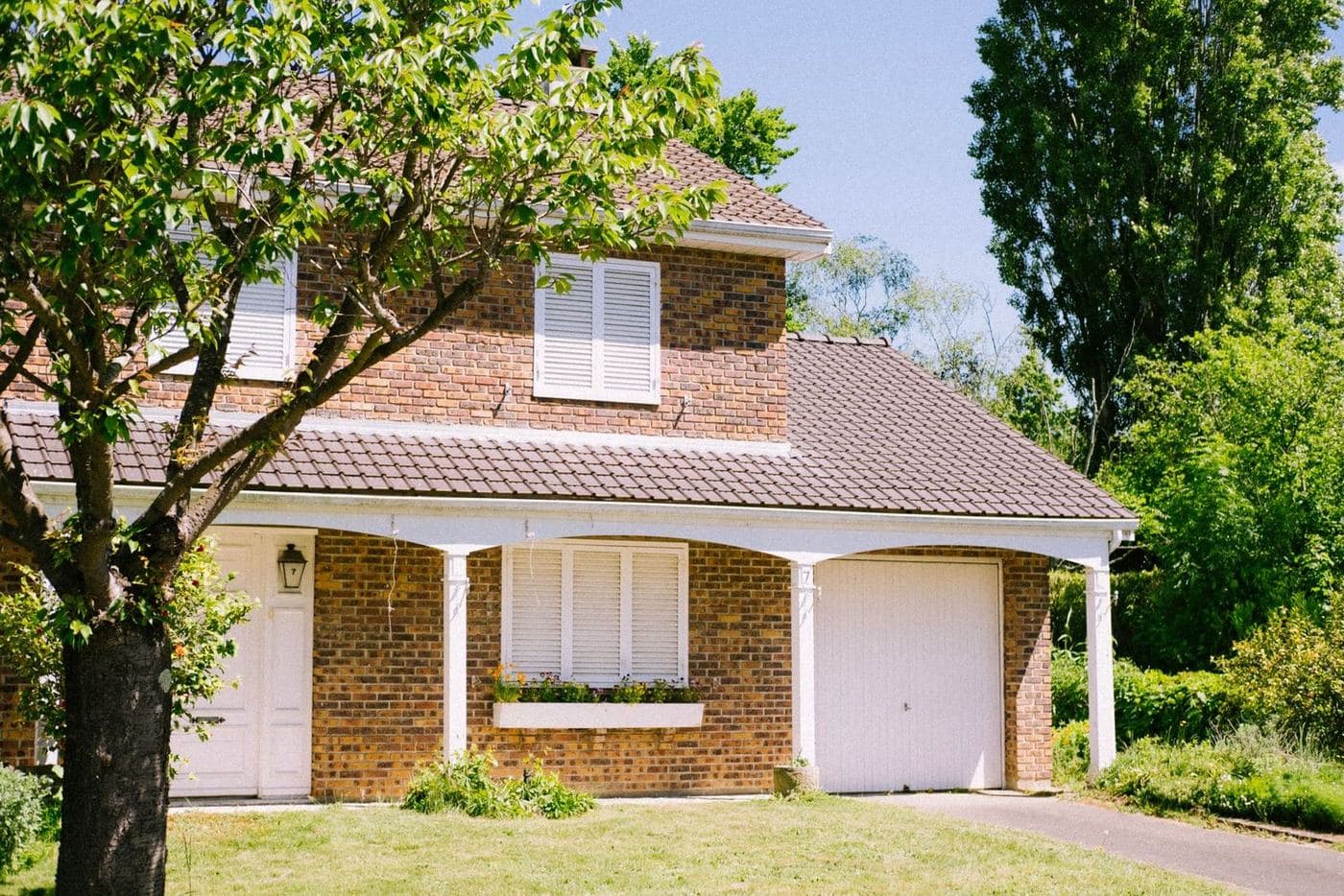 Brick one-and-a-half-story home with a covered carport and a shade tree in the front yard