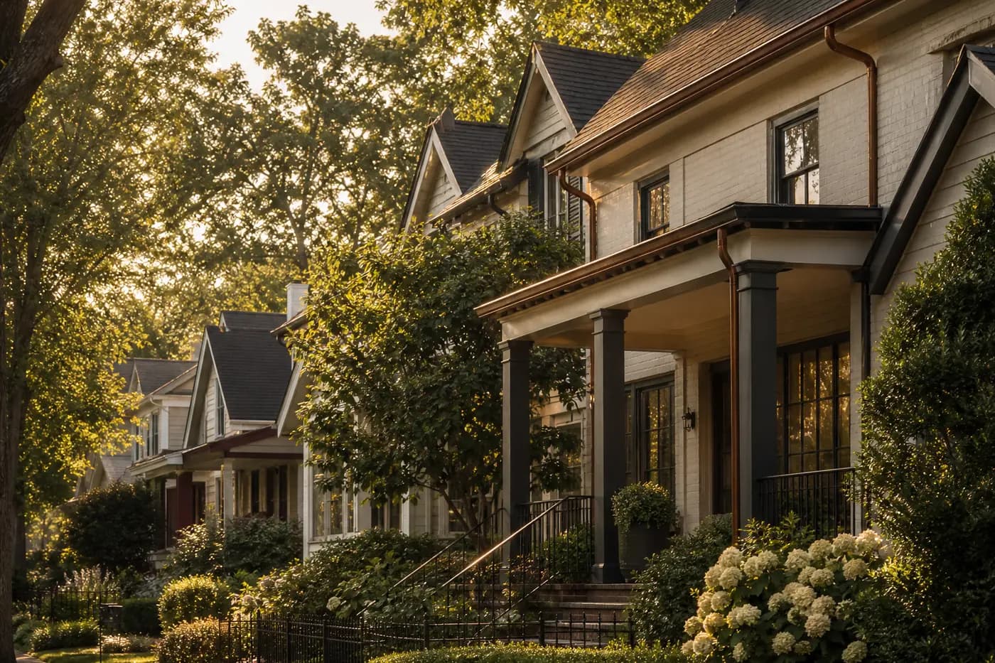 Tree-shaded street of porch-front traditional homes in late-afternoon light