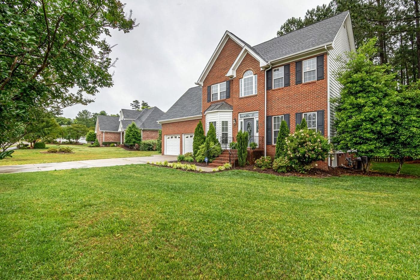 Red-brick two-story traditional home with black shutters and a wide front lawn